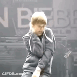 A Man In A Gray Jacket Is Dancing On A Stage In Front Of A Sign That Says Justin Bieber . GIF