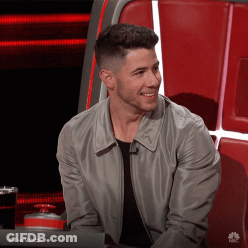A Man In A Gray Jacket Is Smiling In Front Of A Nbc Sign GIF