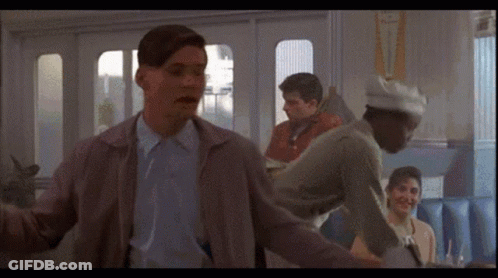 A Man In A Gray Jacket Stands In Front Of A Sign That Says " Fly " GIF
