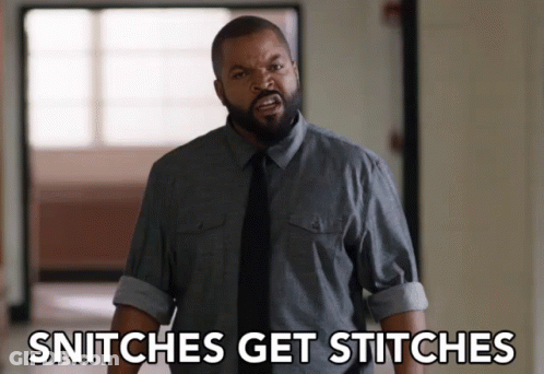 A Man In A Gray Shirt And Black Tie Is Standing In A Hallway And Says Snitches Get Stitches GIF