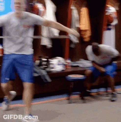 A Man In A Gray Shirt And Blue Shorts Is Dancing In A Locker Room GIF