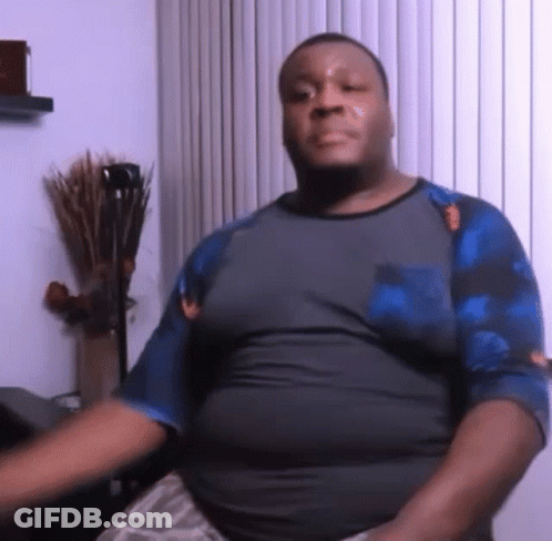 A Man In A Gray Shirt And Blue Sleeves Is Sitting In Front Of A Window . GIF