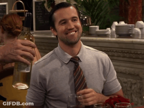 A Man In A Gray Shirt And Tie Holds A Bottle Of Wine GIF