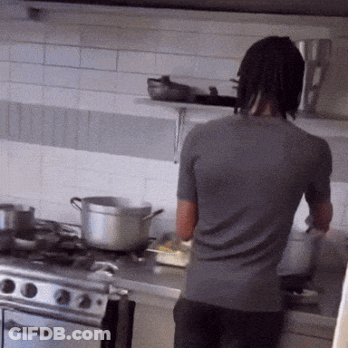 A Man In A Gray Shirt Is Cooking On A Stove GIF