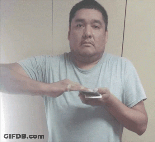 A Man In A Gray Shirt Is Holding A Cell Phone GIF