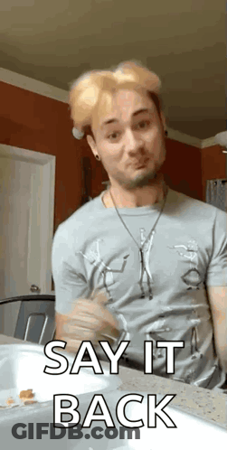 A Man In A Gray Shirt Is Sitting At A Counter And Saying Say It Back . GIF