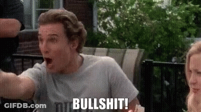 A Man In A Gray Shirt Is Sitting On A Patio With His Mouth Open And A Woman Behind Him . GIF
