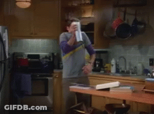 A Man In A Gray Shirt Is Spraying A Can Of Air Freshener In A Kitchen GIF