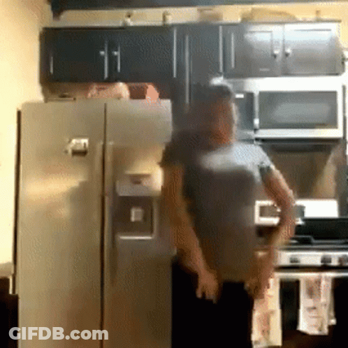 A Man In A Gray Shirt Is Standing In Front Of A Refrigerator In A Kitchen GIF