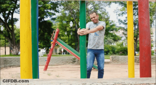 A Man In A Gray Shirt Is Standing In Front Of Colorful Poles GIF