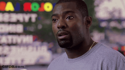 A Man In A Gray Shirt Stands In Front Of A Sign That Says Jojo GIF