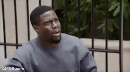A Man In A Gray Sweater Is Sitting In Front Of A Fence And Making A Funny Face . GIF