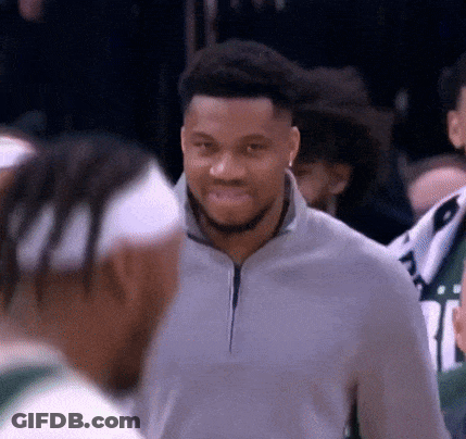 A Man In A Gray Sweater Is Smiling While Talking To Another Man . GIF