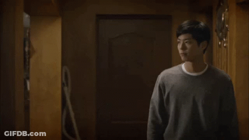 A Man In A Gray Sweater Is Standing In A Room And Talking To Someone . GIF