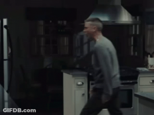 A Man In A Gray Sweater Is Standing In Front Of A Refrigerator GIF