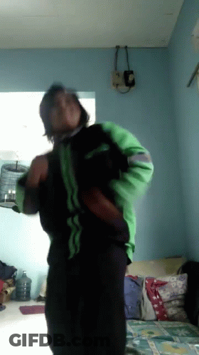 A Man In A Green And Black Jacket Is Dancing In A Living Room GIF