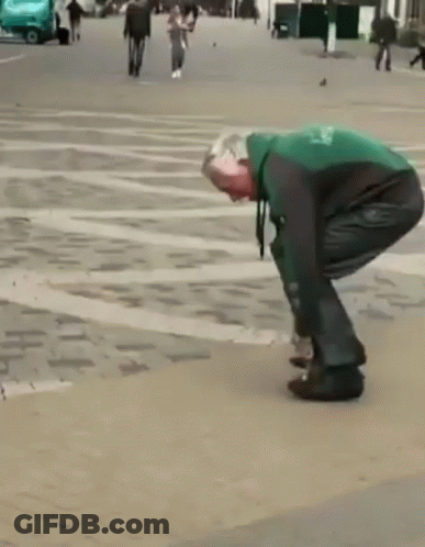 A Man In A Green And Black Jacket Is Tying His Shoes On A Sidewalk GIF