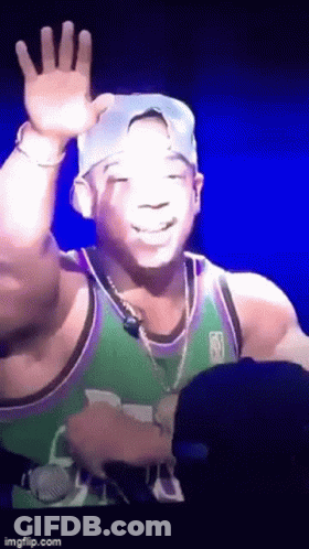 A Man In A Green And Purple Jersey Is Waving At The Camera GIF