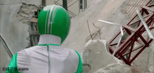 A Man In A Green And White Costume Is Standing In Front Of A Destroyed Building GIF