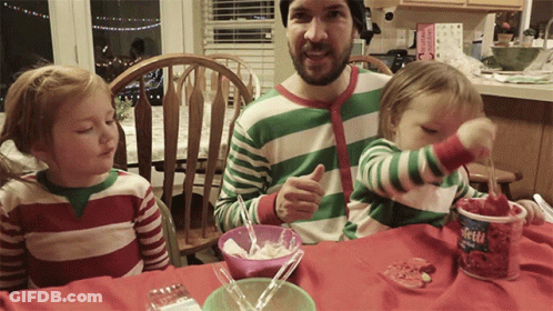 A Man In A Green And White Striped Shirt Is Sitting At A Table With Two Children And A Container Of Strawberry Yogurt GIF