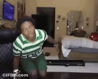 A Man In A Green And White Striped Shirt Is Sitting On A Couch In A Living Room GIF