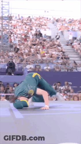 A Man In A Green And Yellow Outfit Is Doing A Handstand In Front Of A Crowd . GIF