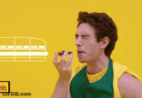 A Man In A Green Apron Eating A Sandwich GIF