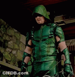 A Man In A Green Arrow Costume Is Holding A Bow And Arrows GIF