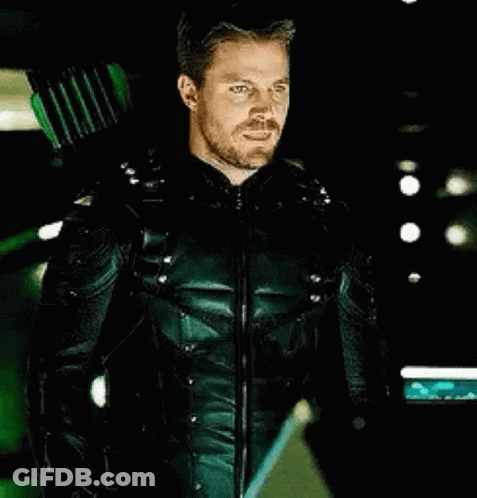 A Man In A Green Arrow Suit Is Holding A Green Arrow Behind His Back . GIF
