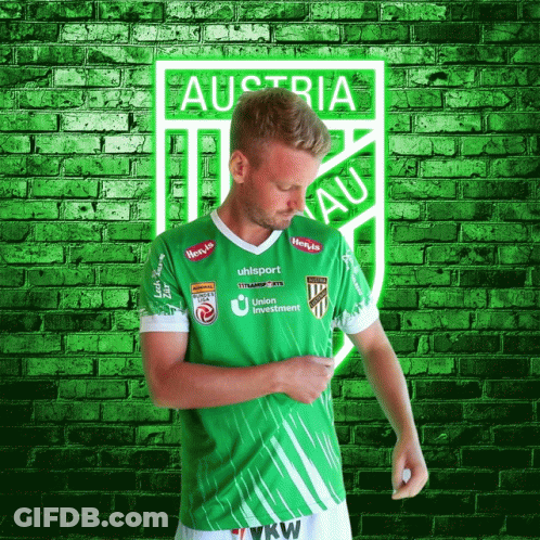 A Man In A Green Austria Jersey Stands In Front Of A Brick Wall GIF