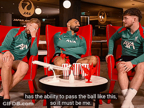 A Man In A Green Axa Shirt Sits In A Red Chair GIF