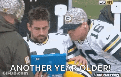 A Man In A Green Bay Packers Uniform Is Talking To Another Man While Holding A Tablet . GIF