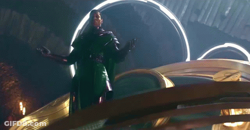 A Man In A Green Cape Is Standing In Front Of A Large Clock GIF