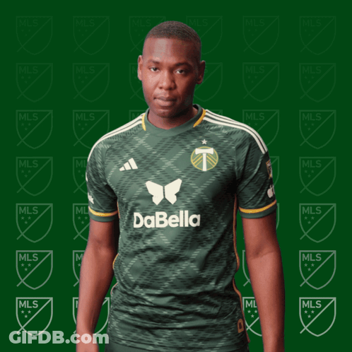 A Man In A Green Dabella Shirt Stands In Front Of A Green Background GIF