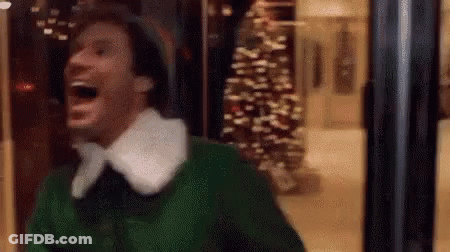 A Man In A Green Elf Costume Is Laughing In A Store Window . GIF