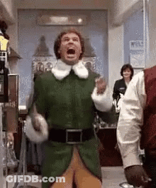 A Man In A Green Elf Costume Is Standing In A Hallway . GIF