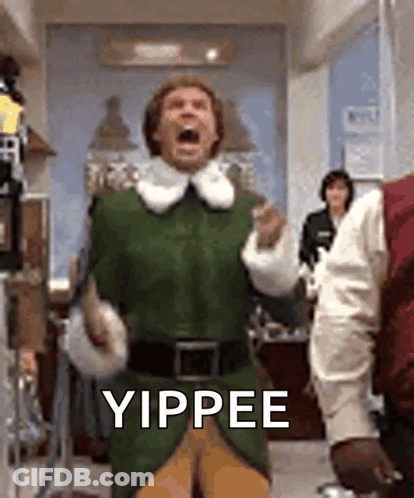 A Man In A Green Elf Costume Is Standing In A Room With His Mouth Open And Yipping . GIF