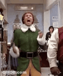 A Man In A Green Elf Costume Is Standing In A Room With His Mouth Wide Open . GIF