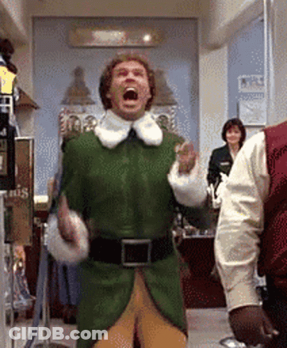 A Man In A Green Elf Costume Is Standing In A Room With His Mouth Wide Open . GIF