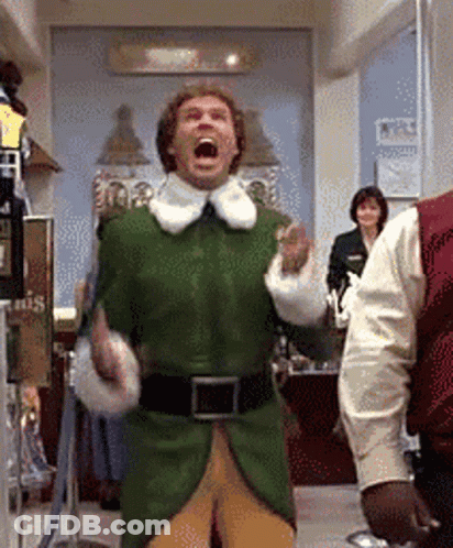A Man In A Green Elf Costume Is Standing In A Room With His Mouth Wide Open . GIF