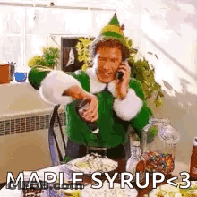 A Man In A Green Elf Costume Is Talking On A Cell Phone While Pouring Maple Syrup Into A Glass . GIF