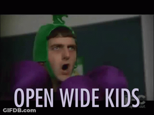A Man In A Green Hat Is Holding Purple Pom Poms And The Words `` Open Wide Kids '' Are Behind Him . GIF