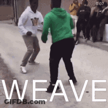 A Man In A Green Hoodie Is Dancing With Another Man In A White Hoodie On A Street . GIF