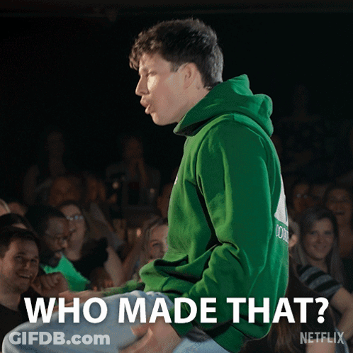 A Man In A Green Hoodie Is Sitting In Front Of A Crowd With The Words " Who Made That " Above Him GIF