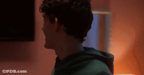 A Man In A Green Hoodie Is Standing In Front Of A Pink Wall GIF