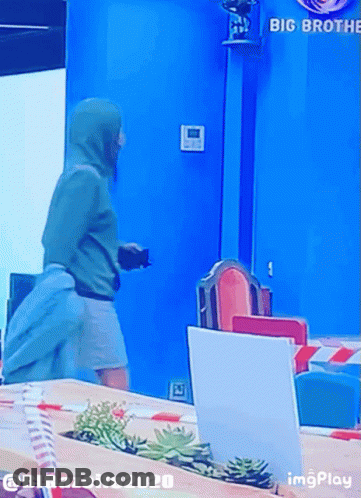 A Man In A Green Hoodie Is Standing In Front Of A Sign That Says Big Brother GIF
