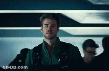 A Man In A Green Jacket And Black Vest Is Standing In A Crowded Room . GIF