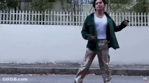 A Man In A Green Jacket And Camo Pants Is Dancing On A Street GIF