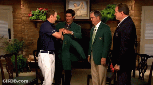 A Man In A Green Jacket Is Being Helped By Another Man In A Blue Shirt GIF
