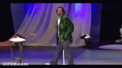 A Man In A Green Jacket Is Dancing On A Stage . GIF